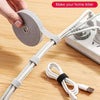 A hand is shown using a reusable hook and loop cable tie to secure wires on a wooden surface.