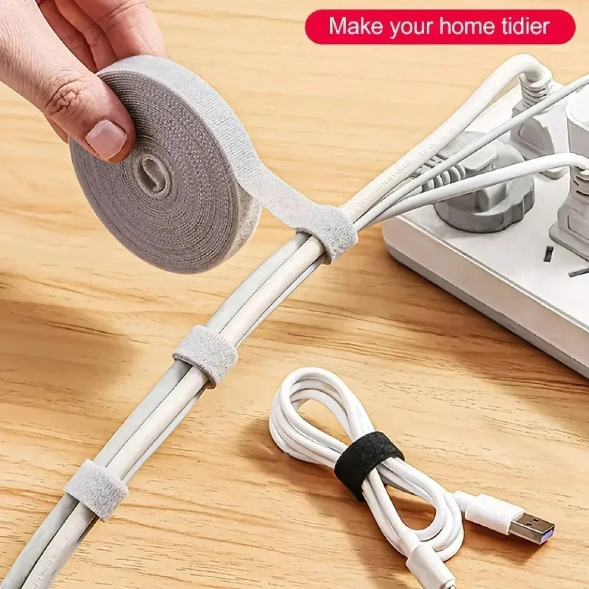 A hand is shown using a reusable hook and loop cable tie to secure wires on a wooden surface.