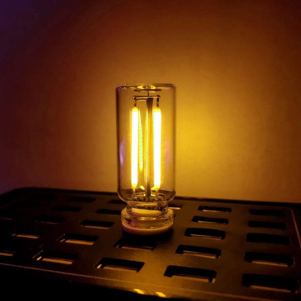 A vintage Edison style LED bulb with a visible filament is displayed on a dark metal surface.
