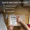 Hands are applying thermal shipping labels onto a cardboard box for printing.