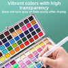 An open watercolor paint set showing various vibrant colors in a palette with a hand holding a brush.
