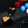 A close-up shot of a black wired in-ear monitor labeled ZERO:2 next to various colored spherical objects.