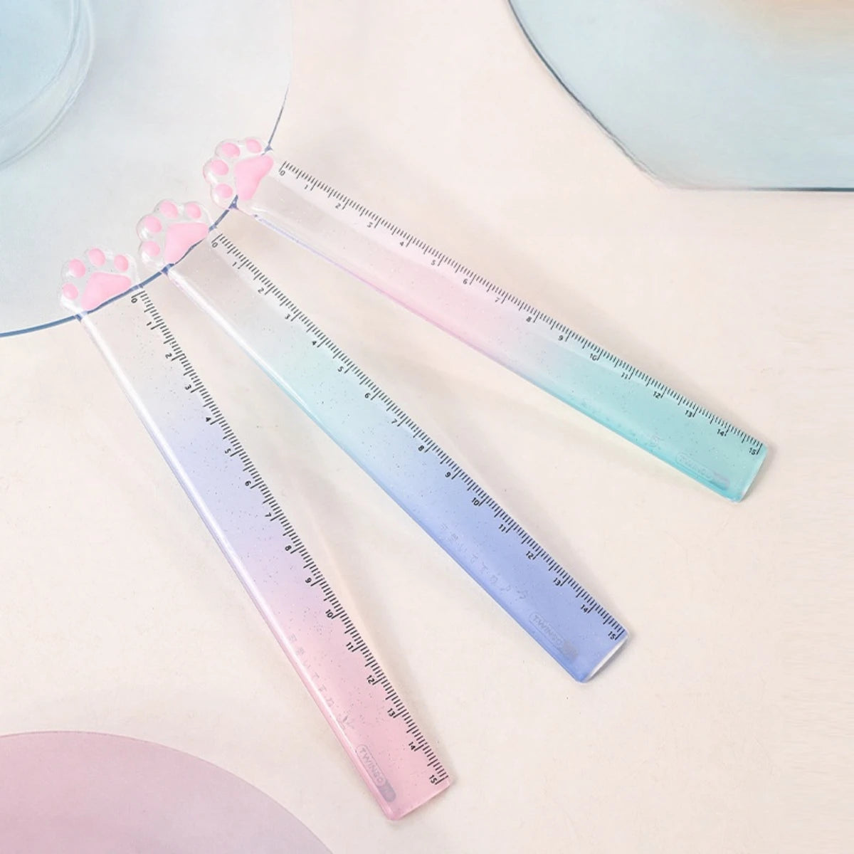 Three transparent plastic rulers shaped like cat paws display a gradient of pink and blue colors.