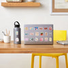 A laptop displaying a colorful cartoon sticker pack on a wooden desk next to a water bottle and pencil holder.