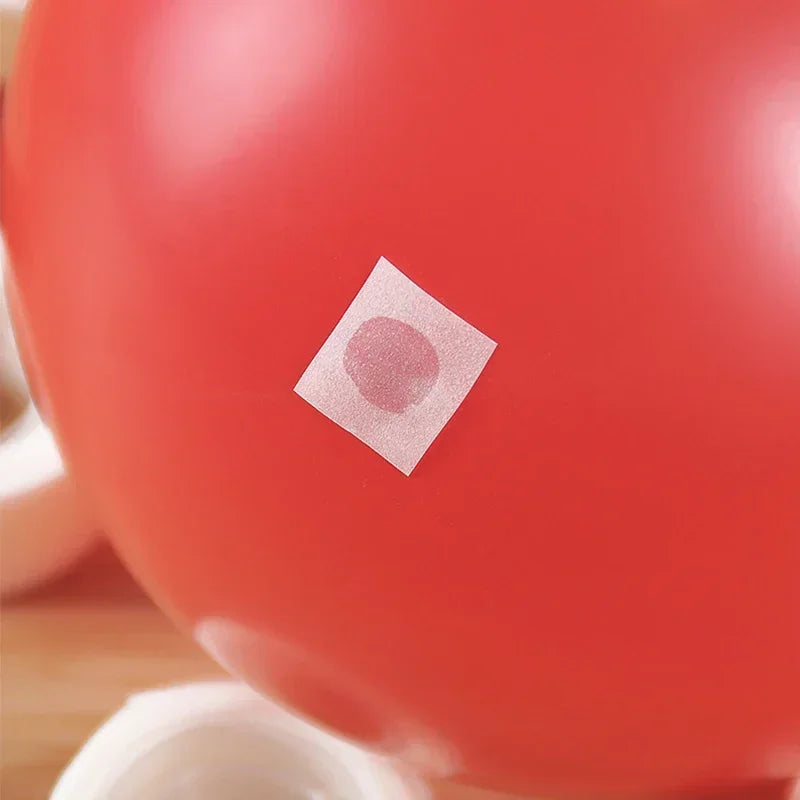 A close-up of a red spherical object with a small, square, pink adhesive dot on its surface.