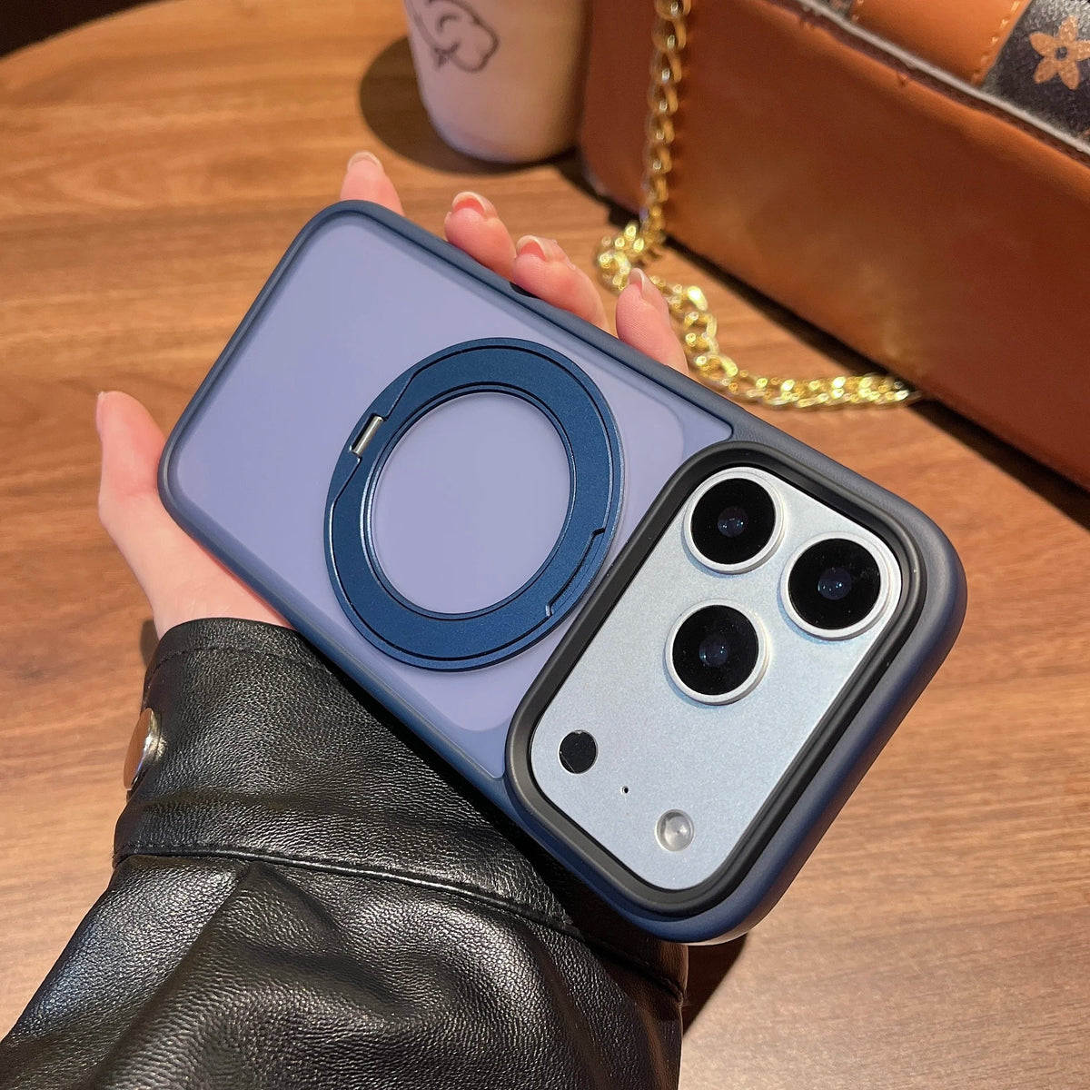 A hand holds a purple magnetic phone case with a rotating ring and multiple camera lenses on a wooden surface.