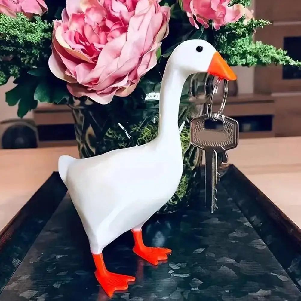 A white ceramic goose figurine with an orange beak standing next to a set of keys on a dark tray.