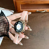 A hand is holding a gold-toned resin beaded watch with a white face and dark bezel on a wooden surface.