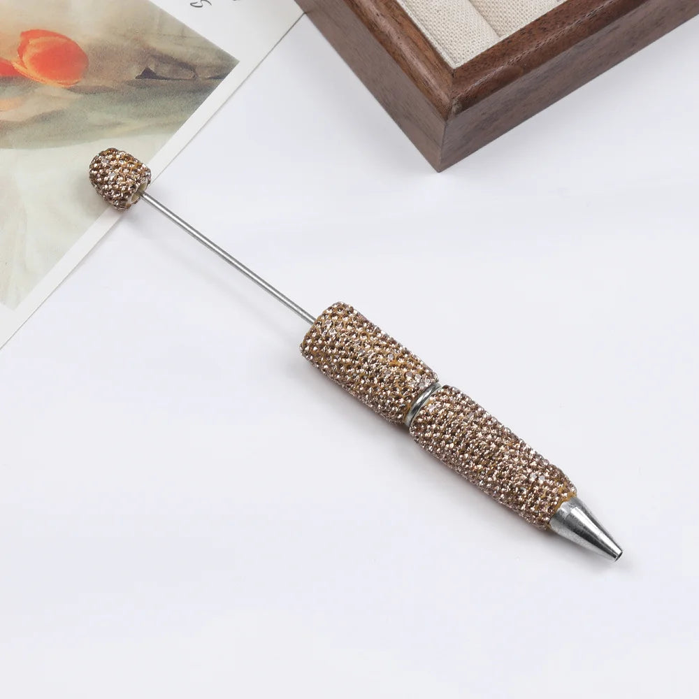 A silver pen accessory featuring a gold-colored beaded tip and a decorative top, displayed on a white surface.