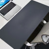 A dark gray oversized gaming mouse pad is shown next to a silver laptop and a portion of a desk setup.