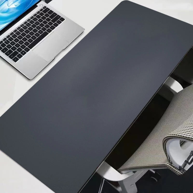 A dark gray oversized gaming mouse pad is shown next to a silver laptop and a portion of a desk setup.