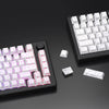 A black keyboard features a set of white PBT keycaps with side-printed legends, including a full keyboard and loose keycaps.