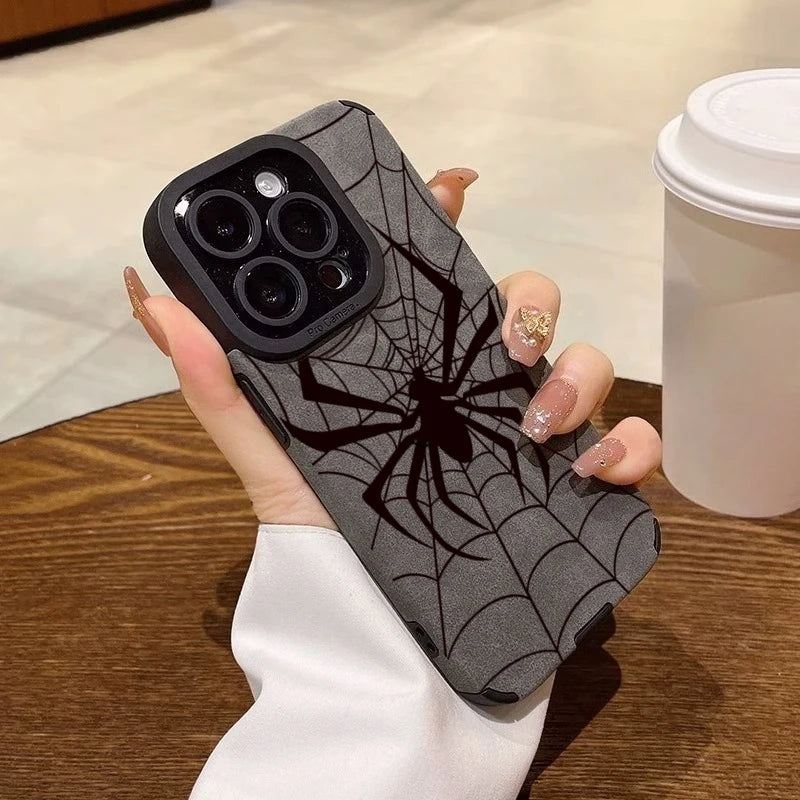A hand holds a black phone case with a black spider web design on a wooden surface.