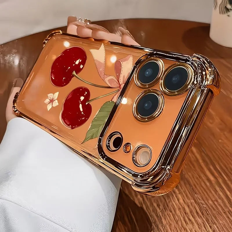 An orange electroplated iPhone case featuring a cherry and leaf pattern, held by a hand.