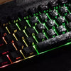 Close-up of a mechanical keyboard with black keycaps and green backlighting showing various letters and symbols.