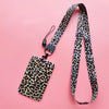 A leopard print ID holder lanyard keychain with a black strap and tag on a pink background.