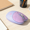 A purple cat-shaped wireless mouse with a pink accent is placed on a light wooden desk next to a notebook and pencils.