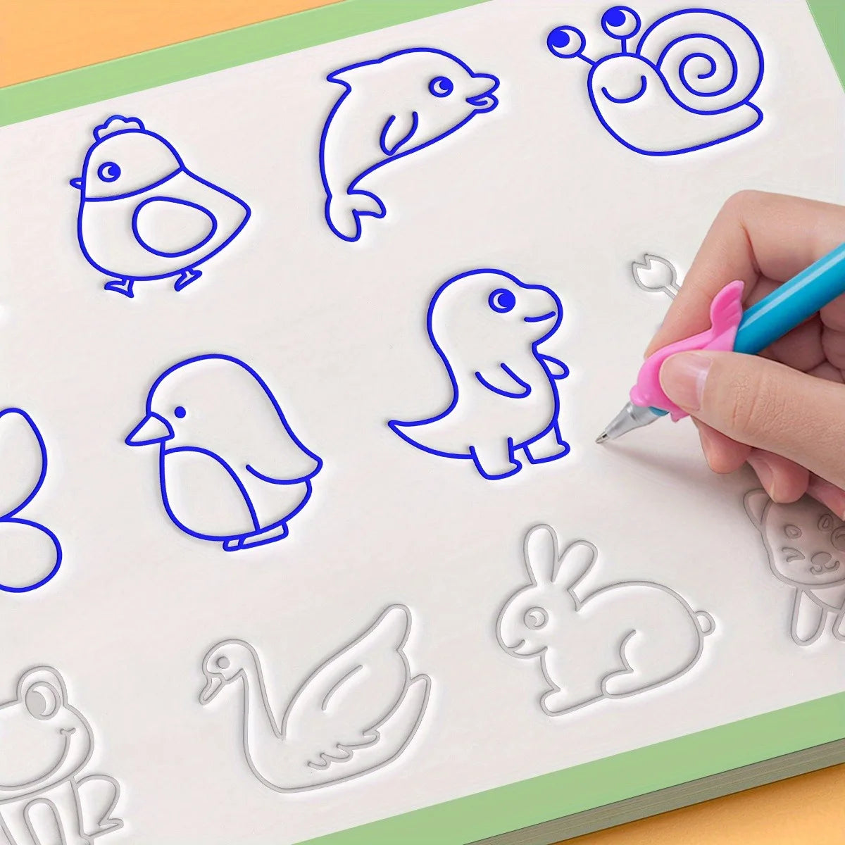 A hand is drawing various animal shapes like a bird, a seal, and a dinosaur on a white practice sheet with blue cutout sticke