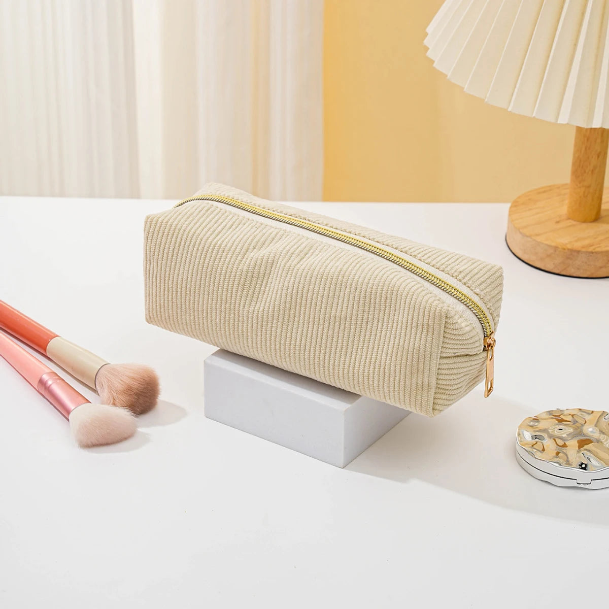 A beige zippered pencil case resting on a white surface next to makeup brushes and a small electronic device.