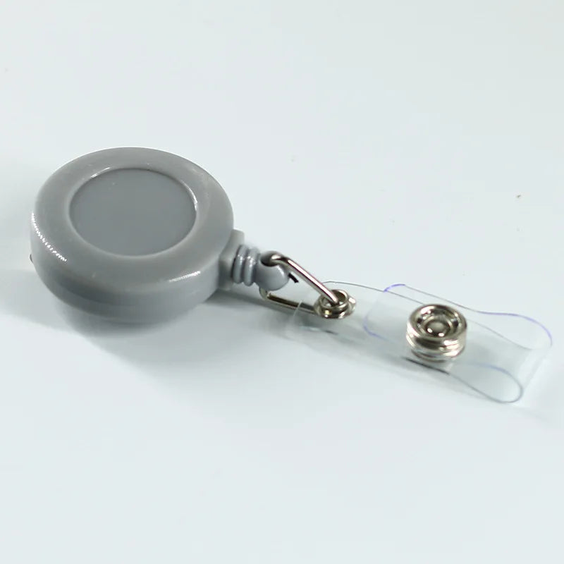 Porta identificación de plástico gris con clip y cordón sujeto a una tarjeta de plástico transparente.