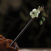 Un délicat accessoire de cheveux en bois floral avec une fleur vert pâle et de petites perles vertes sur un bâtonnet fin.