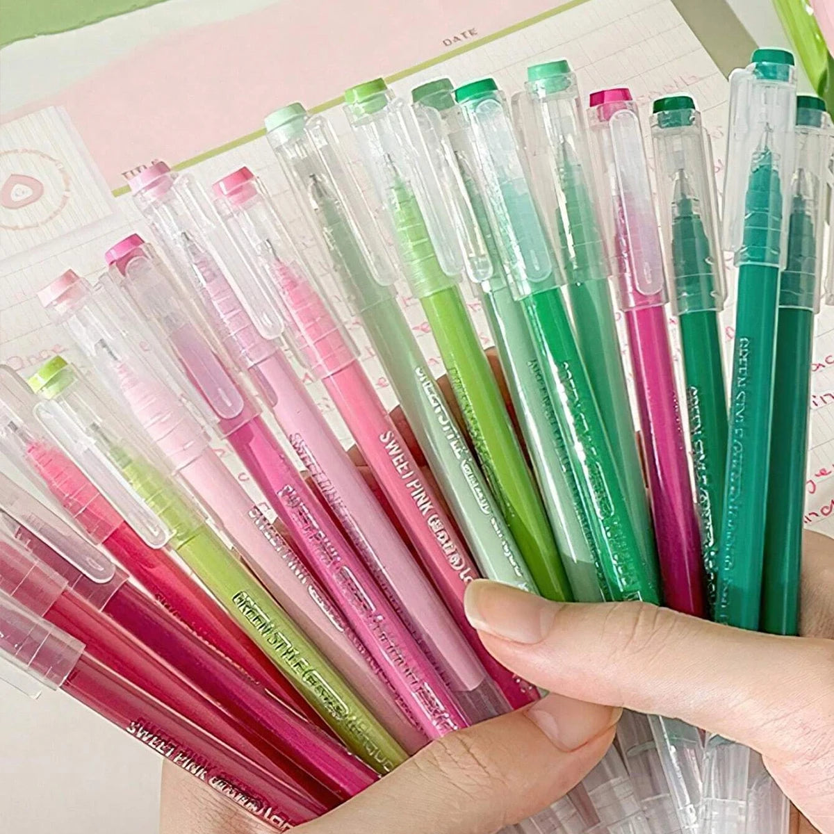 A hand holds a set of multi-color Morandi gel pens in various shades of pink, green, and purple.