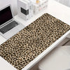 Leopard print XXL gaming mouse pad placed on a white desk next to a laptop and stationery.