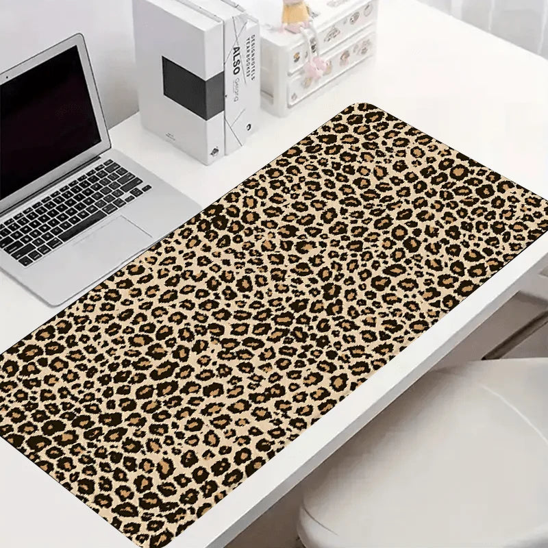 Leopard print XXL gaming mouse pad placed on a white desk next to a laptop and stationery.