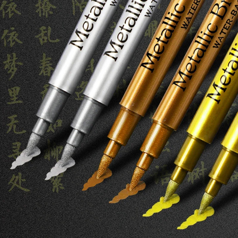 A collection of metallic brush marker pens in various gold and silver colors displayed against a dark background.