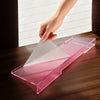 A hand places a clear pink acrylic keyboard riser stand on a wooden desk.
