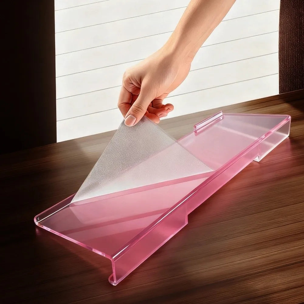 A hand places a clear pink acrylic keyboard riser stand on a wooden desk.
