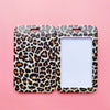 A pair of leopard print ID holders or keychains displayed against a pink background.