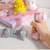 A hand holds a pink ergonomic wrist rest shaped like a pig next to colorful plush toys and a gray cat-shaped rest.