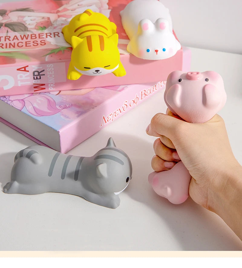 A hand holds a pink ergonomic wrist rest shaped like a pig next to colorful plush toys and a gray cat-shaped rest.