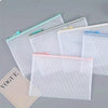 A collection of clear mesh zipper bags in white and pink are displayed on a gray surface.