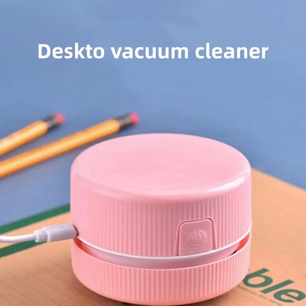 Pinker Mini-Tischstaubsauger neben einem gelben Stift auf Holzoberfläche.