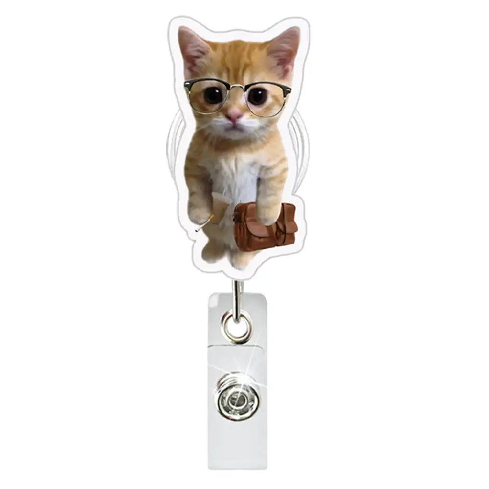 A small orange tabby kitten wearing glasses is clipped onto a retractable ID badge holder with a crocodile clip.