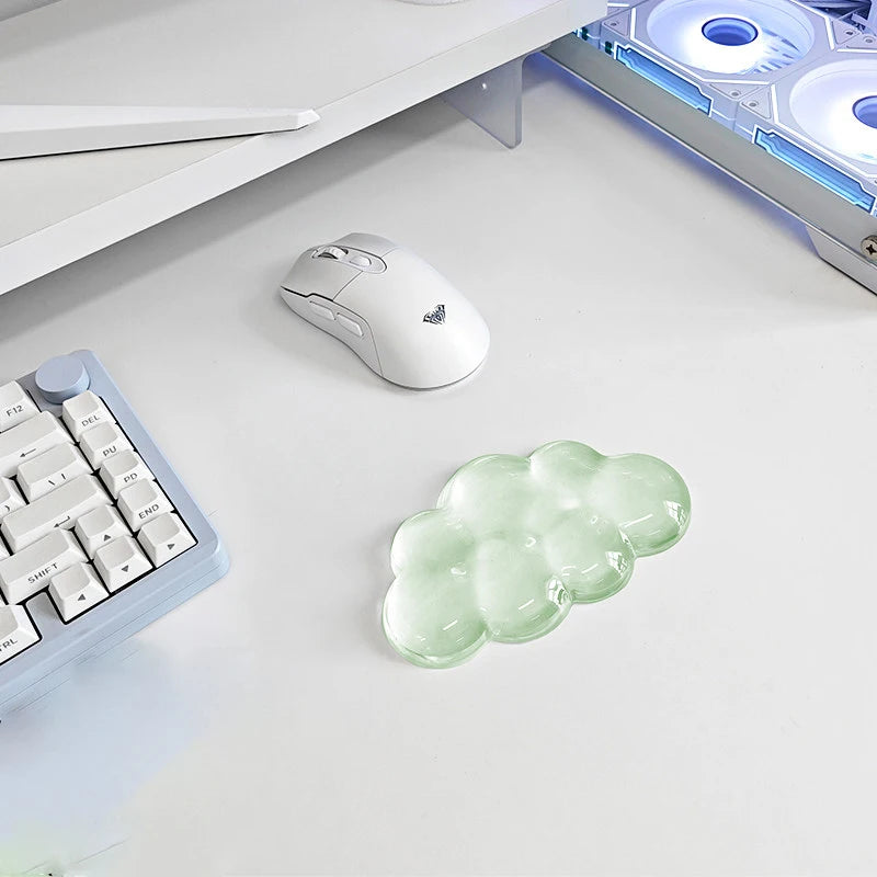 A white ergonomic cloud wrist rest is placed on a white desk next to a white computer mouse and a keyboard.