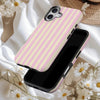 A pink and white striped magnetic dual-layer phone case for an iPhone is shown resting on a light fabric surrounded by white 