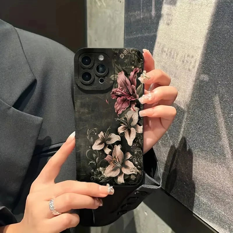 A hand holds a black phone case featuring gothic floral art on an iPhone against a gray background.