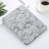 A square silicone skin with gray marble pattern placed on a white surface next to a cup.