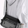 A woman is holding a black multifunctional crossbody bag with a zipper on the front against a light gray background.