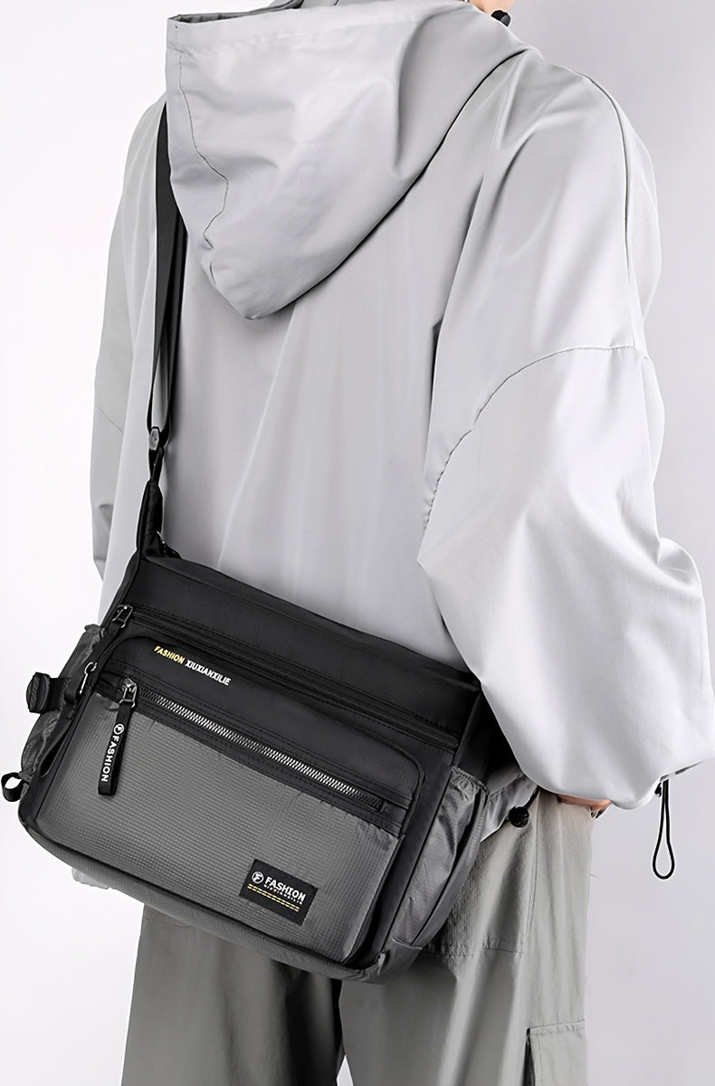 A woman is holding a black multifunctional crossbody bag with a zipper on the front against a light gray background.